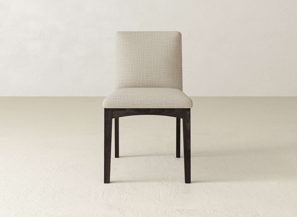 The James & James Klein Dining Chair offers a simple, modern look with a light beige upholstered seat and backrest, paired with dark maple legs. Photographed on an off-white background, it's a stylish choice for any dining area.