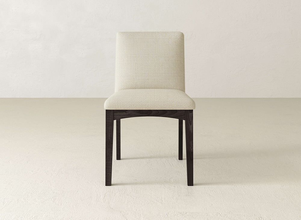 The James & James Klein Dining Chair features a cushioned light beige upholstered seat and back with dark maple legs, offering a modern, simple design that stands out against light floors and off-white walls.