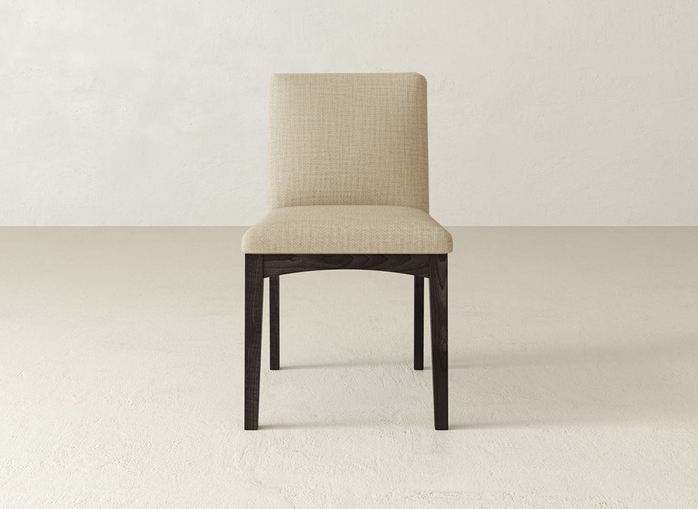 The Klein Dining Chair by James & James features beige upholstery, a straight backrest, and maple wooden legs, set against a plain light-colored wall and floor.