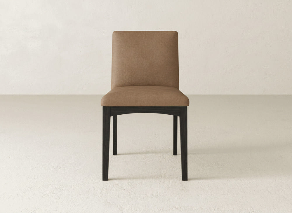 The Klein Dining Chair by James & James features brown upholstery, a straight backrest, and maple wooden legs, shown on a light floor with a plain off-white wall backdrop.