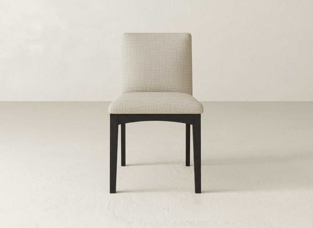 The James & James Klein Dining Chair features a light textured fabric seat and backrest with dark maple wooden legs, shown against a plain light-colored wall and floor.