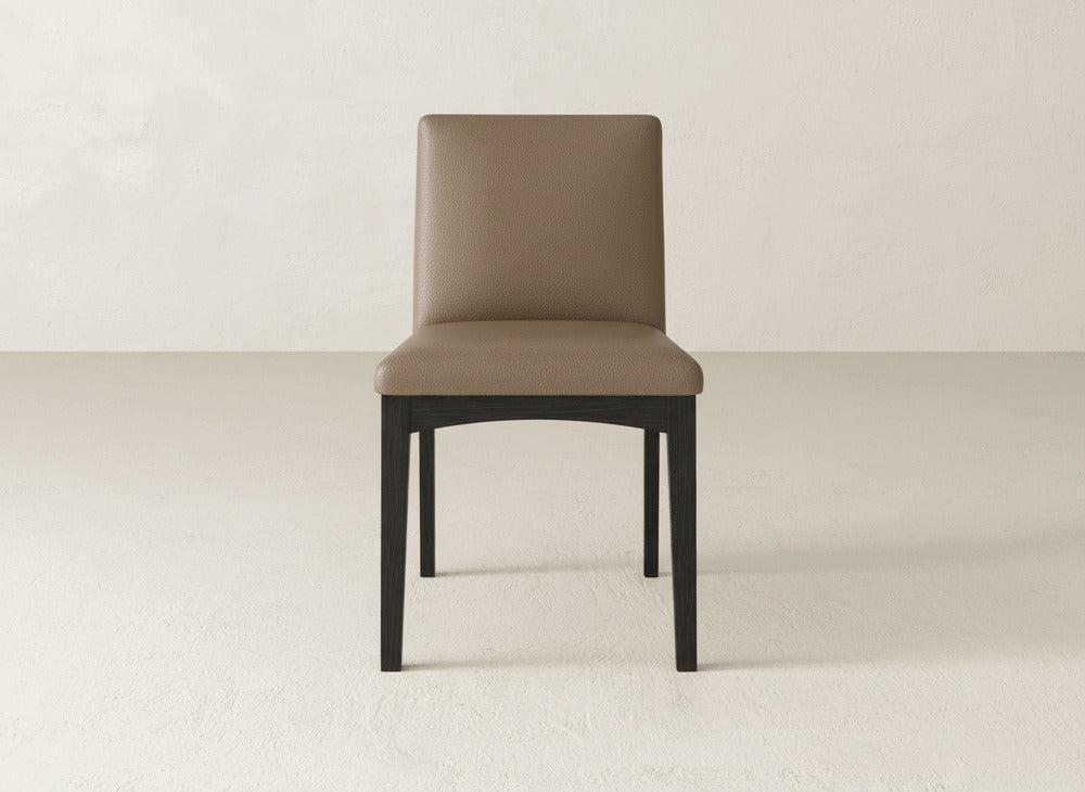 The James & James Klein Dining Chair showcases a modern design with a brown cushioned seat and backrest, paired with black maple legs. It stands out on a light floor against an off-white wall.