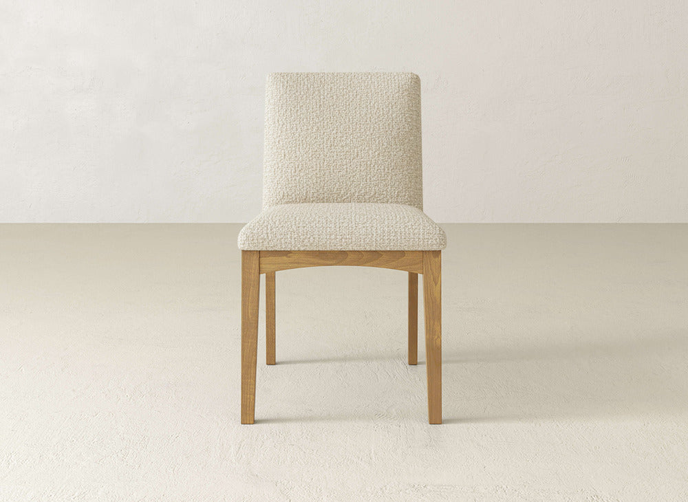 The Klein Dining Chair by James & James has a light wood frame, maple legs, and a textured cream upholstered seat and back, shown on a neutral floor with a plain light wall.