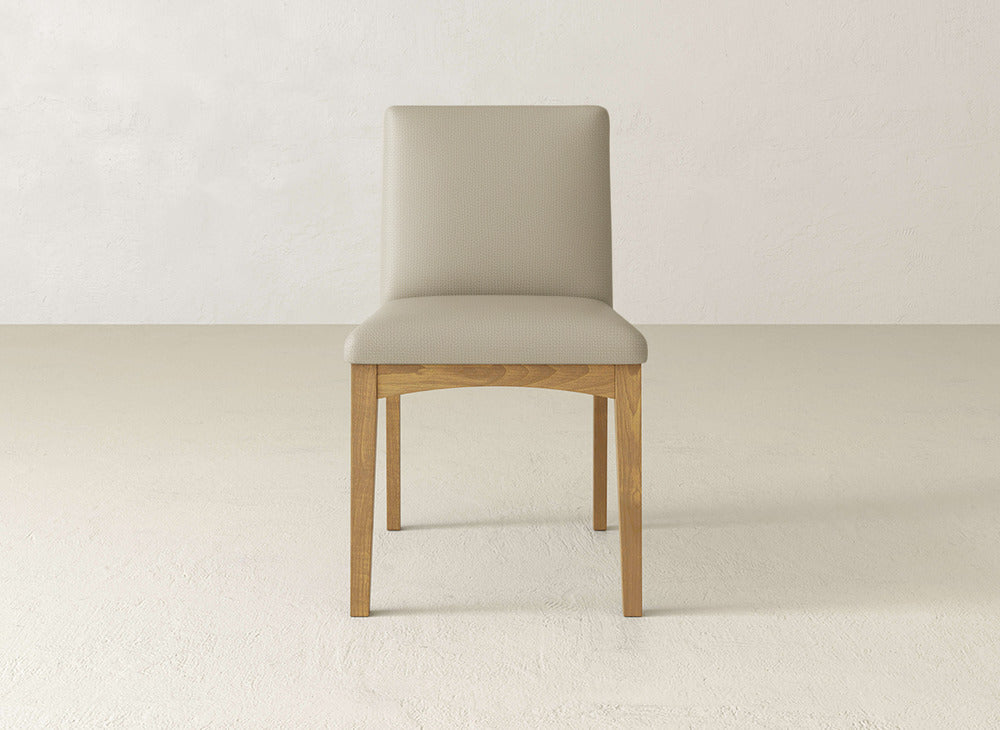 The James & James Klein Dining Chair features minimal, modern design with maple wooden legs and a light beige upholstered seat and backrest, shown against a simple, light-colored background.