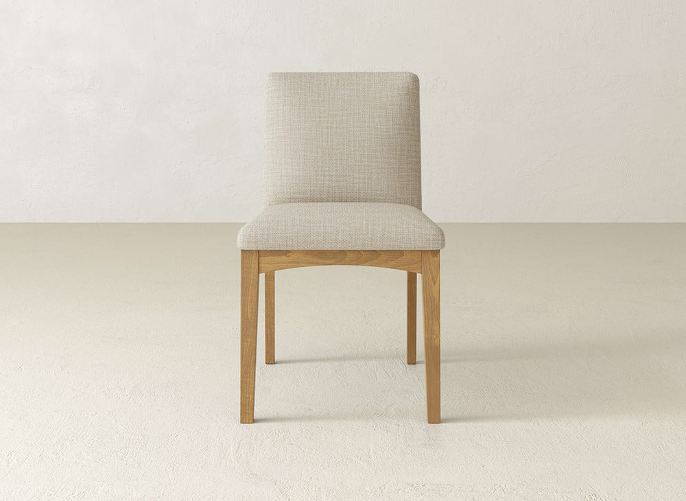 The James & James Klein Dining Chair showcases maple legs and a light beige upholstered seat and backrest, set front-facing on a neutral floor against an off-white wall.