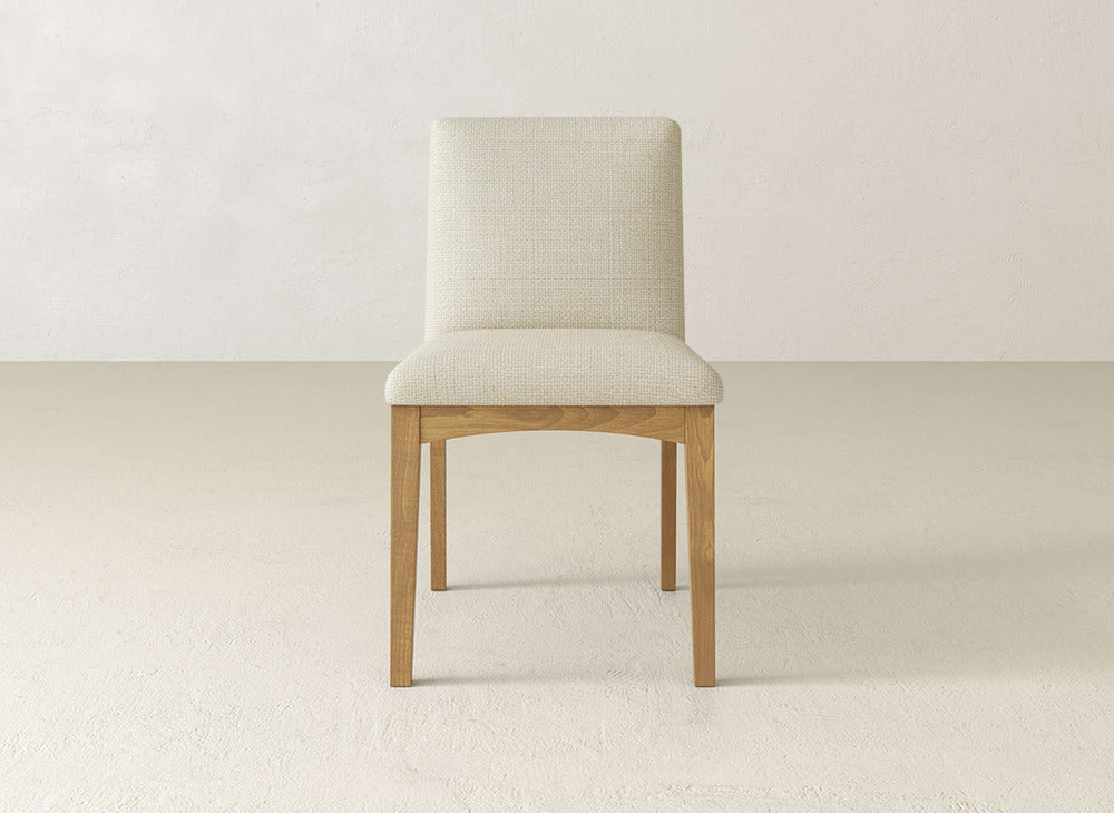 The James & James Klein Dining Chair showcases maple legs with a light beige upholstered seat and backrest, set against a plain, light background.
