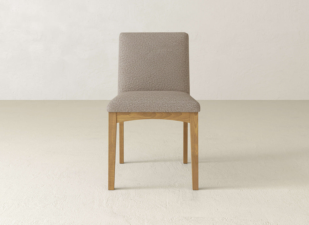 The Klein Dining Chair by James & James features a light brown upholstered seat and backrest with maple wooden legs, shown on a light floor against a plain off-white wall.