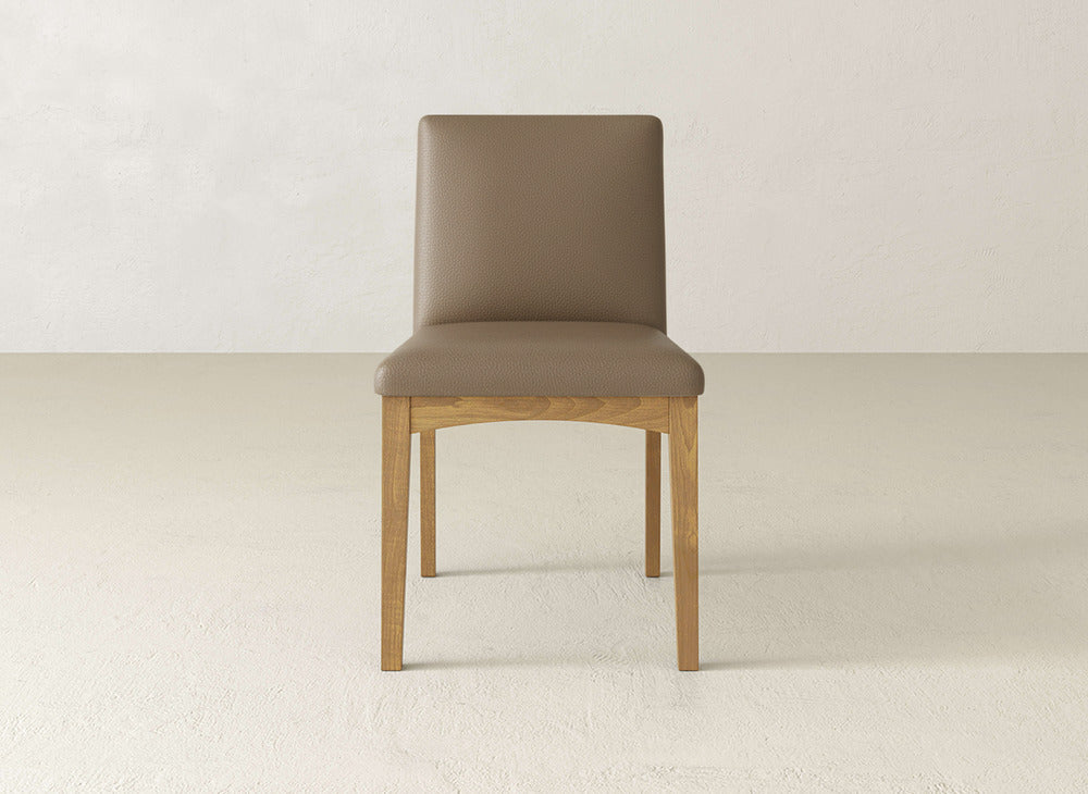 The Klein Dining Chair by James & James features maple wooden legs and a light brown upholstered seat and backrest, shown on a light floor against an off-white wall.