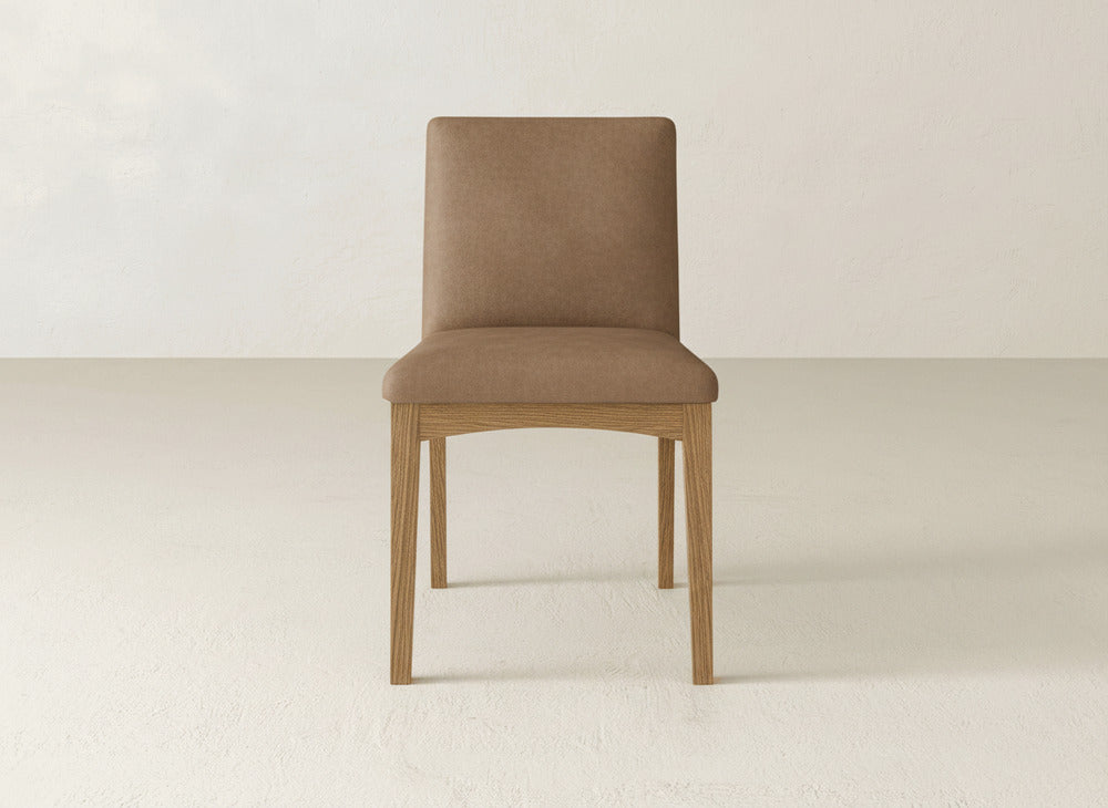 A James & James Klein Dining Chair with brown upholstery and maple wood legs is centered in a minimal, light-toned room with plain textured walls and floor.