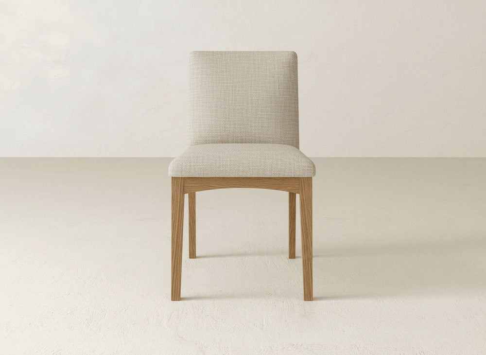 The James & James Klein Dining Chair features a light beige upholstered seat and backrest with straight maple wooden legs, shown on a minimalist background.
