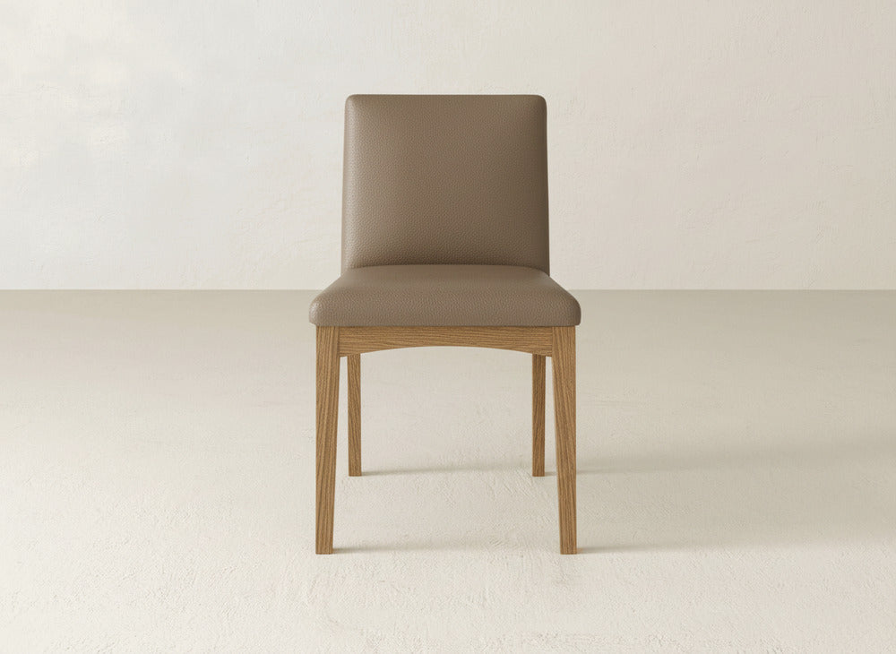 The Klein Dining Chair by James & James features a light brown upholstered seat and backrest with four sturdy maple legs, displayed on a light floor against an off-white wall.