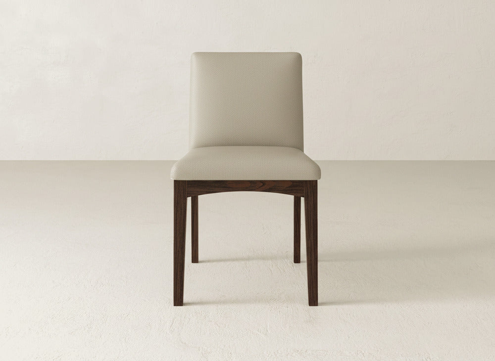The James & James Klein Dining Chair features a modern design with light beige upholstery on the seat and backrest, supported by four straight maple wood legs, shown against a plain off-white background.