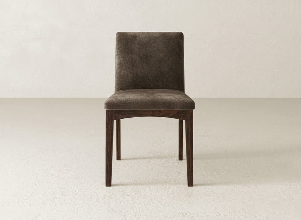 The James & James Klein Dining Chair features a dark brown upholstered seat and backrest, four straight maple legs, and is shown on a light plain floor against a neutral textured wall.