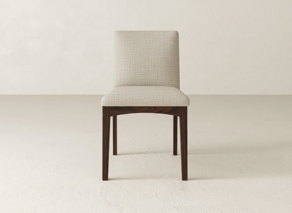The Klein Dining Chair by James & James showcases a light beige upholstered seat and back with elegant dark maple legs, set on a light floor against an off-white wall.