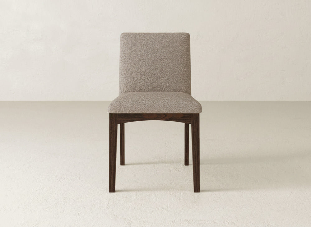 The Klein Dining Chair by James & James features a modern upholstered design with a textured beige seat and backrest, dark maple wooden legs, and is ideal for minimal, light-colored spaces.