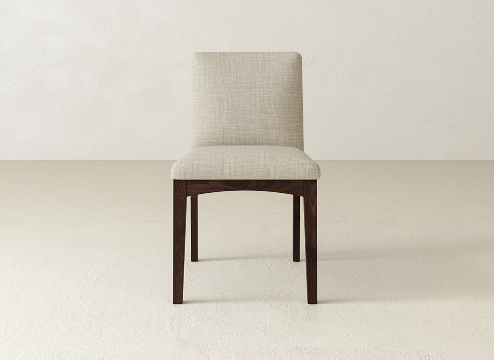 The Klein Dining Chair by James & James features a beige upholstered seat and backrest with elegant maple legs, perfectly accentuating a light floor and plain light wall.