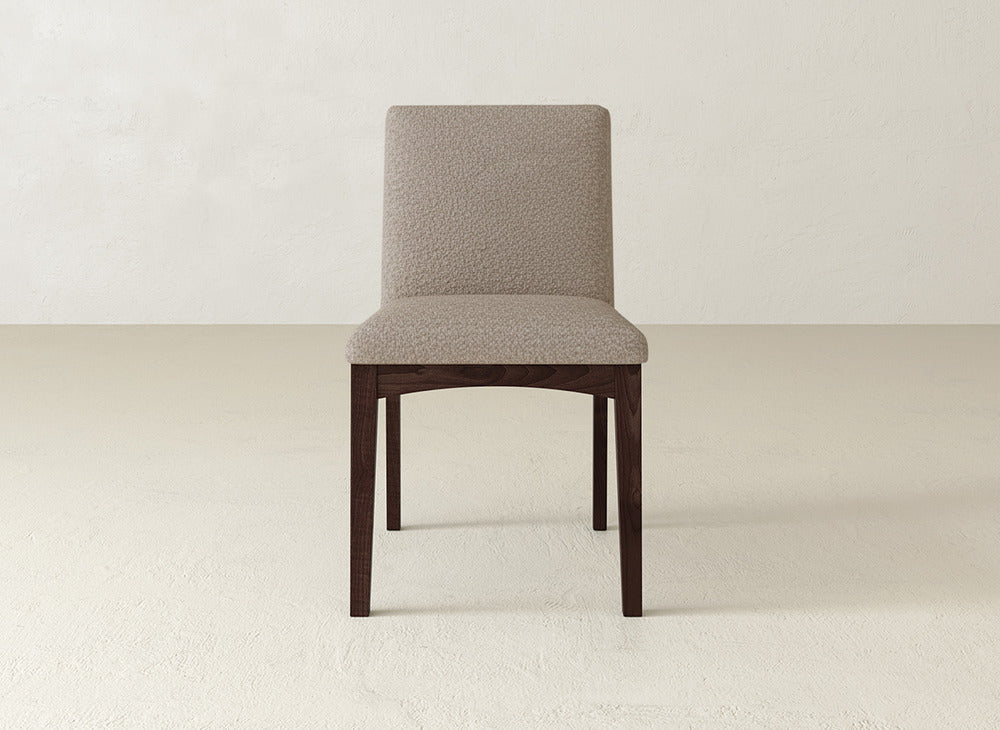 The Klein Dining Chair by James & James features a beige upholstered seat and backrest with dark maple legs, shown on a light textured floor against a plain light wall.