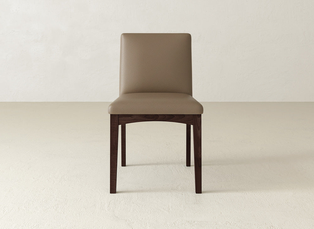 The Klein Dining Chair by James & James features a light brown upholstered seat and backrest with elegant maple wooden legs, shown in an empty room with light-colored walls and floor.