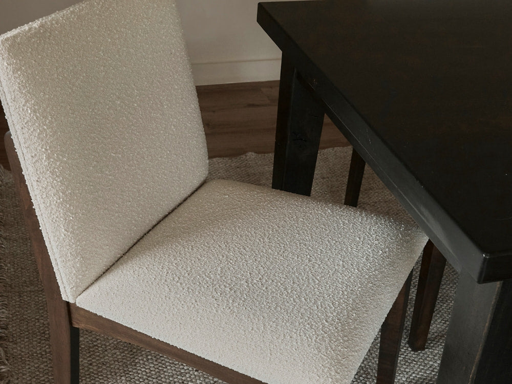The Bisque - Boucle Swatch chair from James+James, featuring white bouclé upholstery and dark wooden legs, sits by a matching table on a woven rug, adding casual elegance and soft texture to the space.