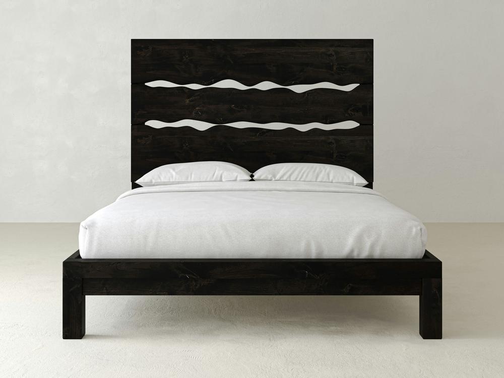 The James+James Live Edge Bed in Charred Ember on Alder features a modern dark wood frame with a high headboard and two wavy horizontal cutouts, topped with white bedding and two pillows, set against a light-colored wall.