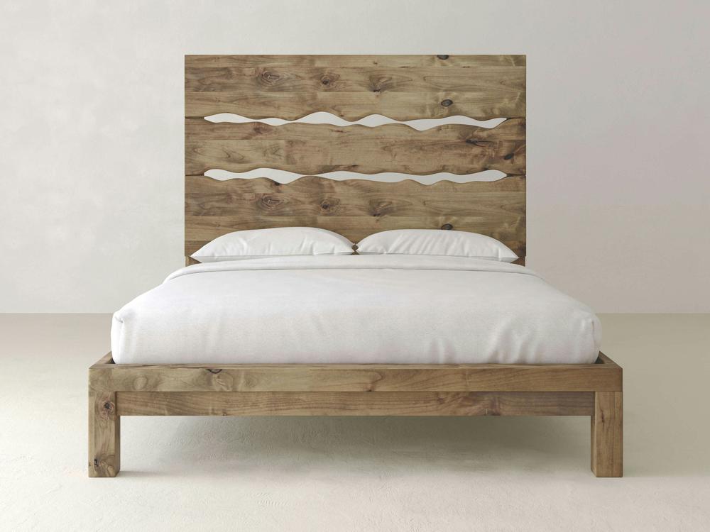 The James+James Live Edge Bed - Harvest Wheat on Alder features a tall, rustic headboard with three wavy cutouts, topped with white pillows and simple bedding, set against a light-colored wall and floor.