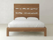 The James+James Live Edge Bed - Almond on Oak features a high headboard with three wavy cutouts, shown here with white bedding and two pillows against a plain, light-colored background.