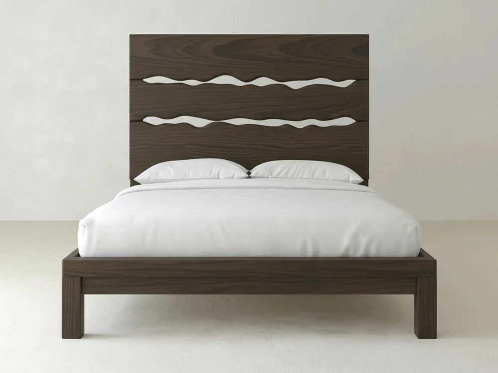 The James+James Live Edge Bed – Espresso on Oak features a tall, dark brown headboard with three wavy cut-out designs, dressed in white bedding and pillows, set against a plain light-colored wall and floor.