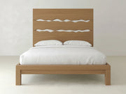 The James+James Live Edge Bed - Oat on Oak is a wooden bed frame with a tall headboard featuring three wavy cut-out designs, styled with white pillows and bedspread against a plain white wall.
