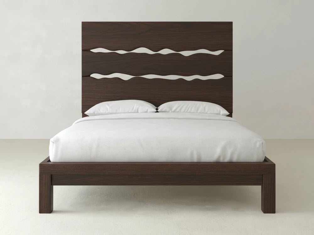 The Live Edge Bed - Sable on Oak by James+James features a modern dark wood design with a tall headboard accented by three horizontal wavy cut-outs, styled here with crisp white bedding and pillows against a light wall and floor.