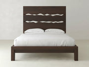 The Live Edge Bed - Sable on Oak by James+James features a modern dark wood design with a tall headboard accented by three horizontal wavy cut-outs, styled here with crisp white bedding and pillows against a light wall and floor.