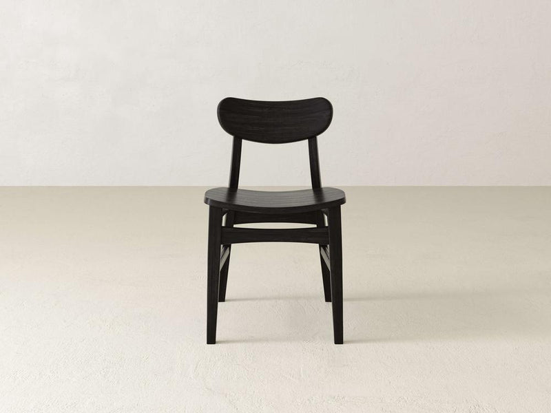 Introducing the Lynn Dining Chair in Tobacco by James+James, an exquisite piece that boasts a dark brown wooden frame with a sophisticated curved backrest. This minimalist, modern design features a slightly curved seat for enhanced comfort and showcases simple, clean lines without armrests. The chair is positioned facing slightly to the right, offering a glimpse of its elegant back view.