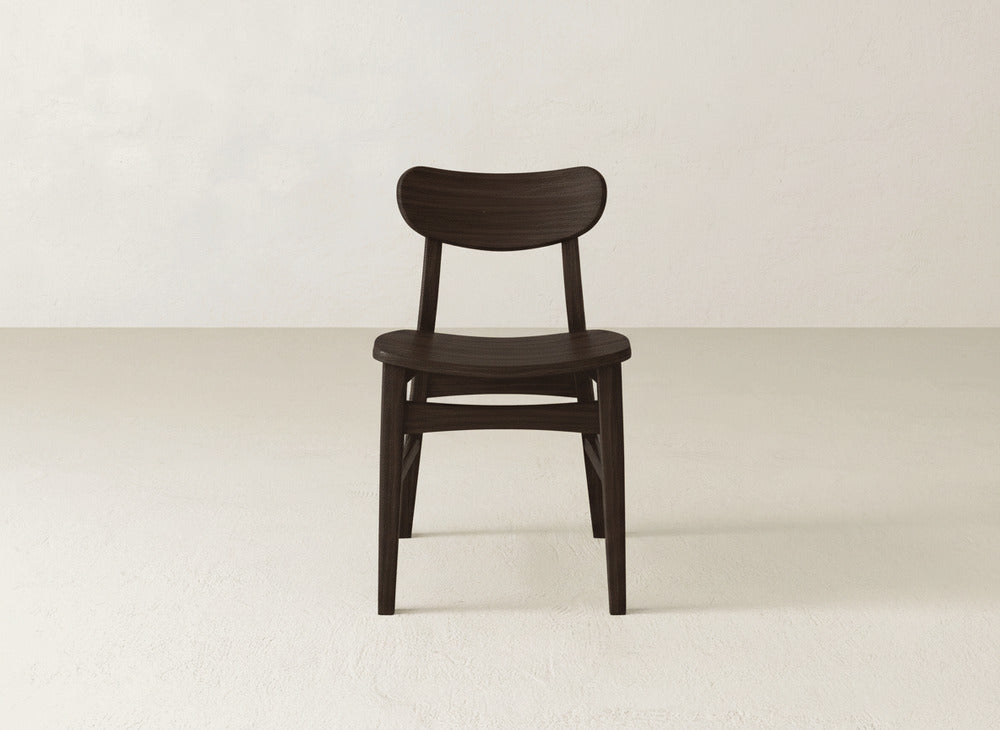 The James+James Lynn Dining Chair, crafted from solid maple hardwood with a curved backrest and minimalist design, features a dark wood finish and is shown on a light floor against an off-white wall.