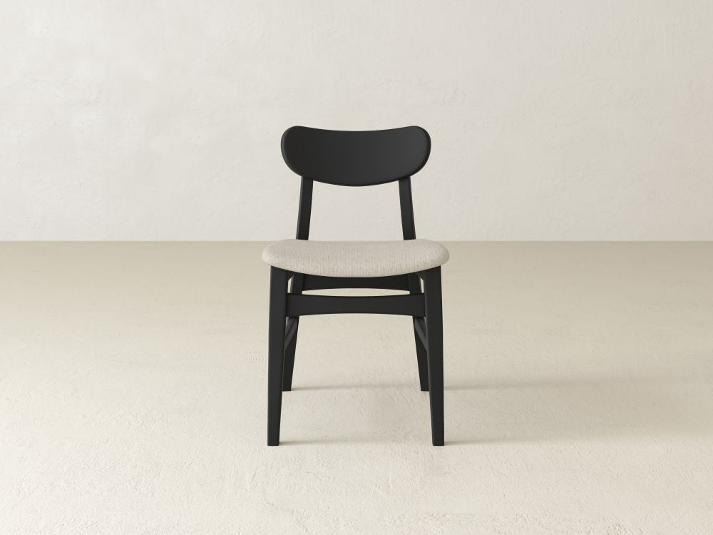 The Lynn Upholstered Dining Chair by James+James is a simple black dining chair made from maple wood, featuring a light gray cushioned seat on an off-white background. Its slightly curved backrest adds modern sophistication.