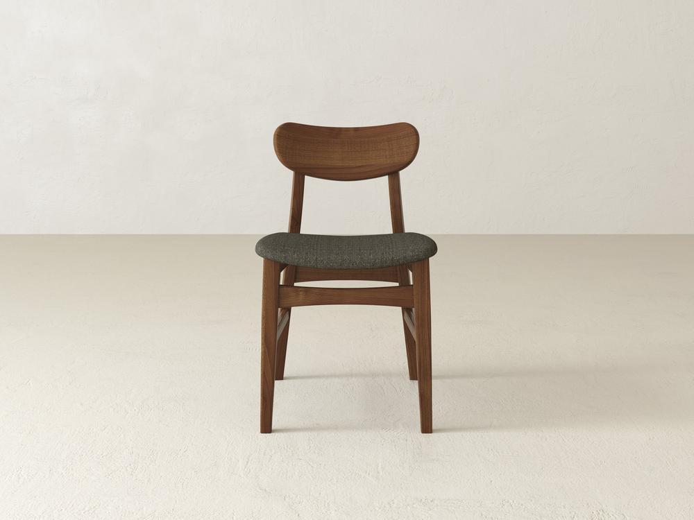 A wooden chair with a curved backrest and dark gray cushioned seat is centered in a minimalist, light-colored room. The floor and walls are a soft, neutral shade.
