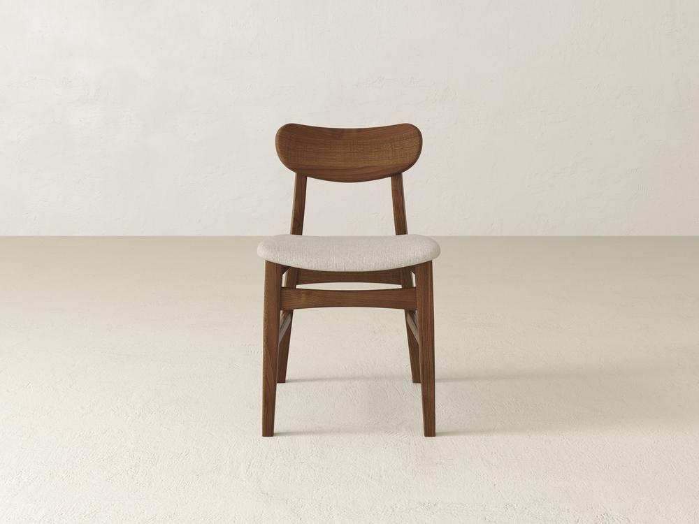 A wooden chair with a curved backrest and a light gray cushioned seat is centered in a minimalistic, off-white room.