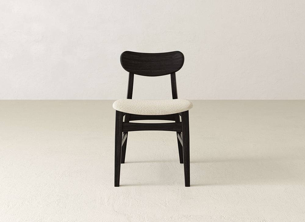 The Lynn Upholstered Dining Chair by James+James features modern sophistication with a dark maple wood frame and light upholstered seat, standing elegantly on a light floor against an off-white wall.