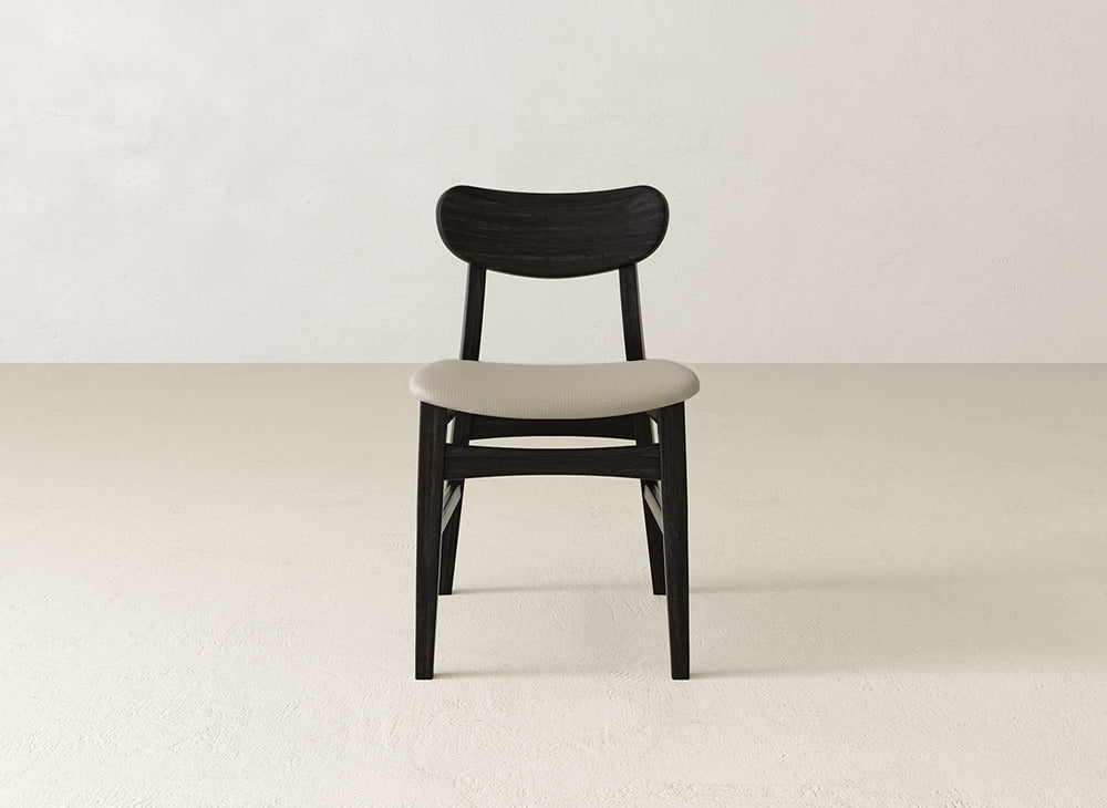 The Lynn Upholstered Dining Chair by James+James features a curved backrest and light cushioned seat in maple wood, adding modern sophistication to minimal spaces with bright floors and walls.