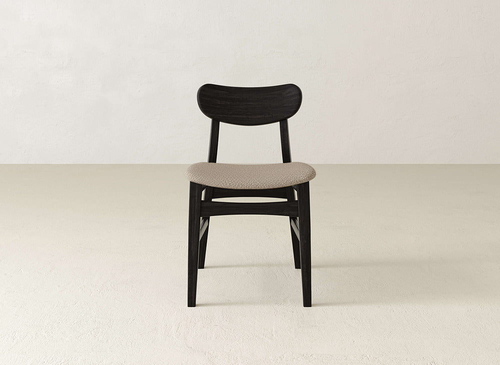 The Lynn Upholstered Dining Chair by James+James features a curved dark maple backrest and legs, complemented by a light beige upholstered seat, perfect for adding modern sophistication to any dining space.
