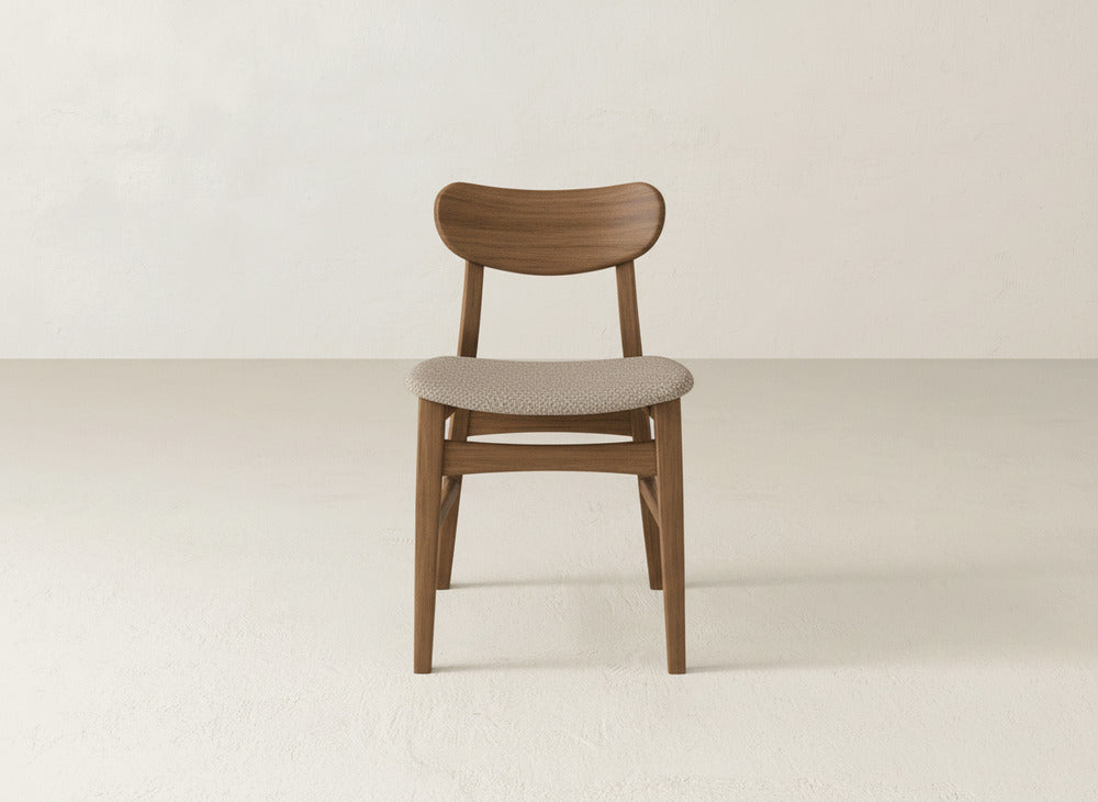 The Lynn Upholstered Dining Chair by James+James, crafted from maple with a curved backrest and light upholstery, adds modern sophistication to a minimalist space with off-white walls and floors.
