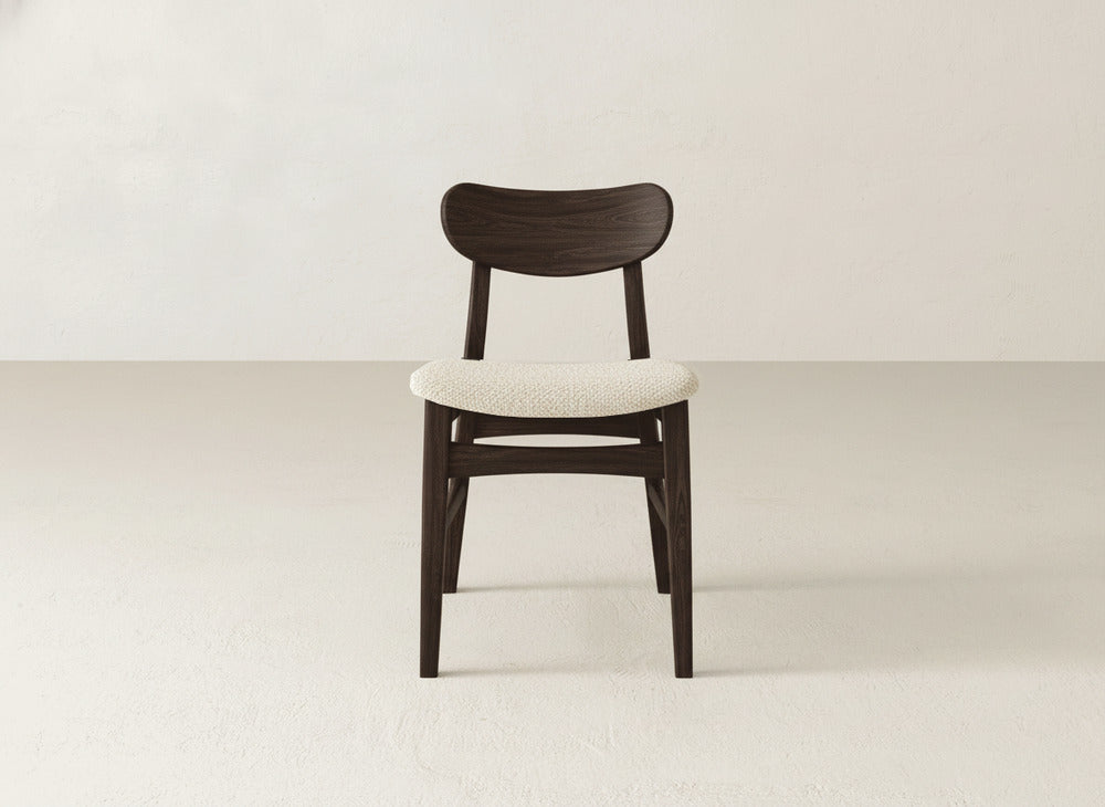 The Lynn Upholstered Dining Chair by James+James features a maple wood frame, rounded backrest, and light cream cushion, offering modern sophistication on a light floor against an off-white wall.