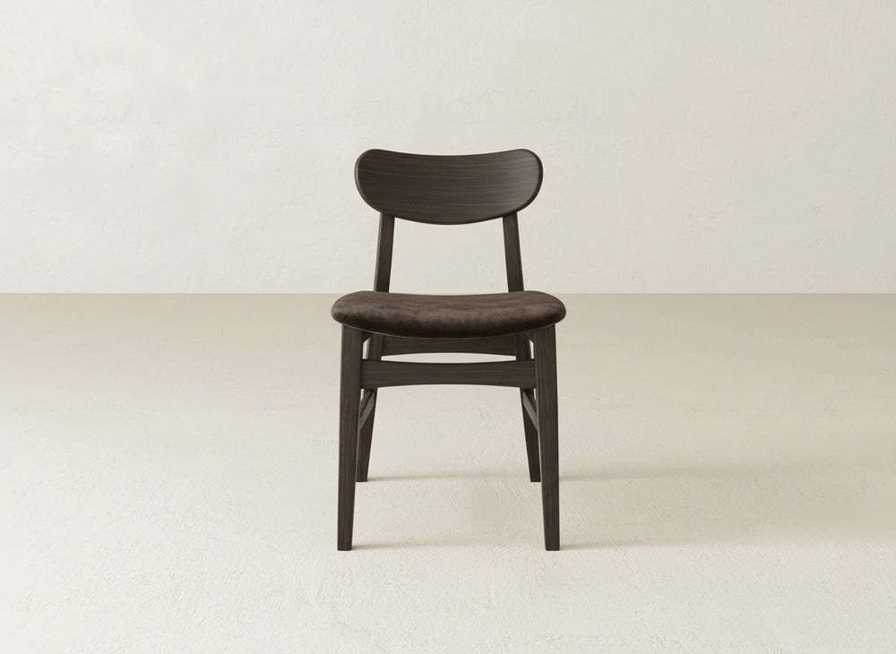 The Lynn Upholstered Dining Chair by James+James features a dark maple wood frame, curved backrest, and padded seat, set against an off-white background—a simple yet refined choice for modern dining spaces.