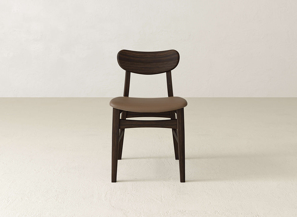 The James+James Lynn Upholstered Dining Chair showcases modern style with a curved dark backrest, light brown cushioned seat, and maple wood construction—perfect for contemporary spaces.