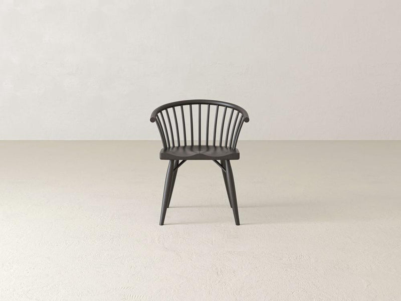 A dark wooden chair with a curved backrest and vertical slats, featuring four tapered legs, is positioned against a plain white background. The chair has a minimalist and modern design.