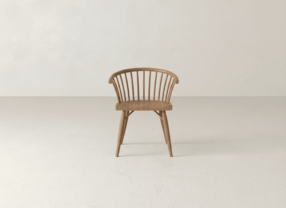 The James+James Maria Dining Chair, crafted from solid maple with a curved backrest and vertical slats, is centered in a minimalist, light-toned room.