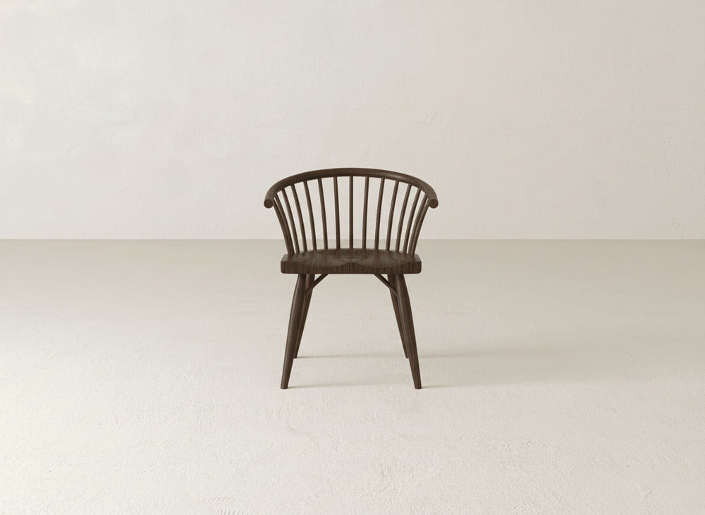 The Maria Dining Chair by James+James, featuring a Shaker-inspired design with a spindled backrest and curved arms, is displayed front-facing on a light floor against an off-white wall.