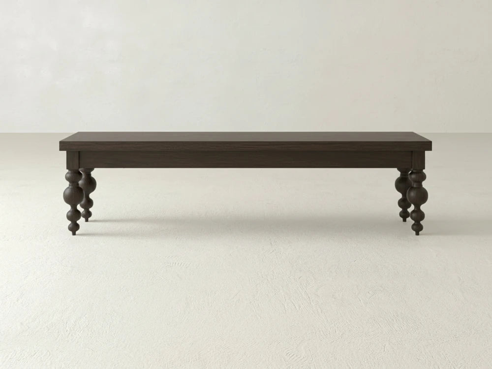 The James+James Olivia Bench in Espresso on Oak, featuring ornate turned legs, stands on a light textured floor against a plain off-white wall.