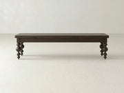The Olivia Bench - Sable on Oak by James+James features dark wood and ornate, rounded legs, standing on a light floor against a plain off-white wall.