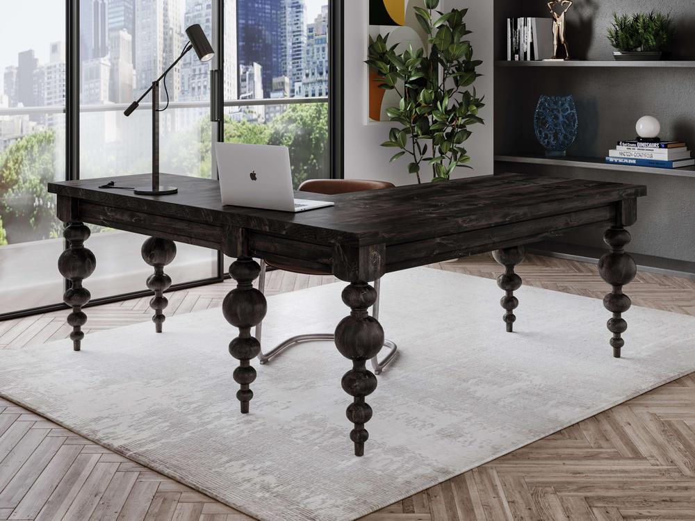 A modern office setup featuring the sturdy "Olivia Corner Desk - Charred Ember" by James+James with ornate legs. A laptop, lamp, and book sit on the desk. The floor has a light-colored rug and herringbone wood pattern. Large windows offer a city view, and a plant and shelves provide additional decor.