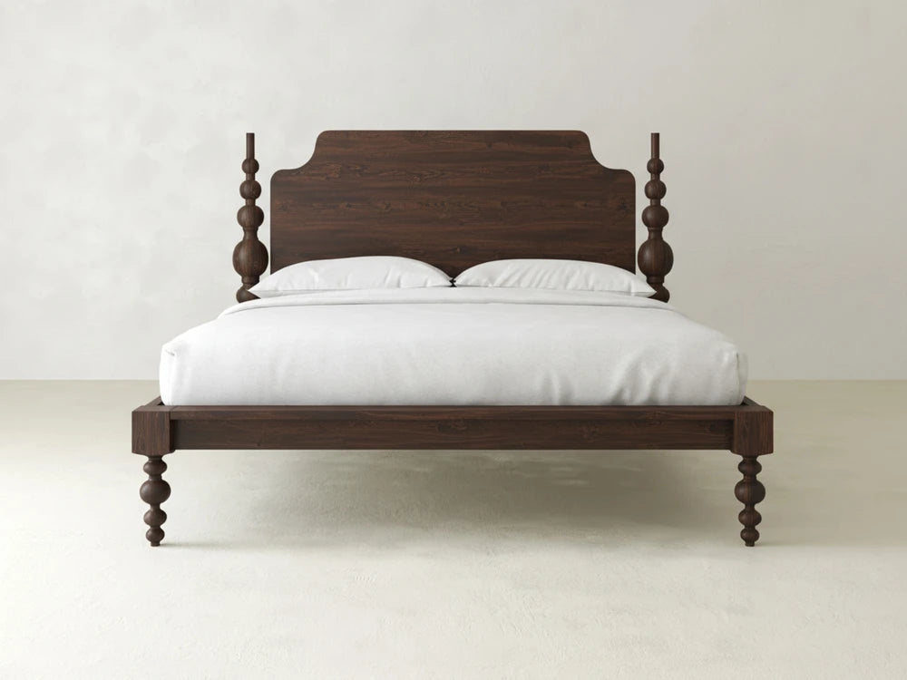 The Olivia Poster Bed - Sable on Oak by James+James features dark wood with turned posts and a tall headboard, paired with white bedding and two pillows, set against a simple, light wall and floor.