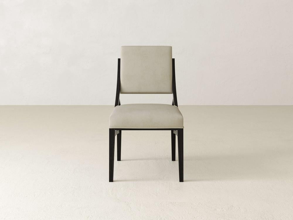 A minimalist chair with a beige cushioned seat and backrest is centered against a plain, light-colored background. The chair features clean lines and a modern design with a black frame.